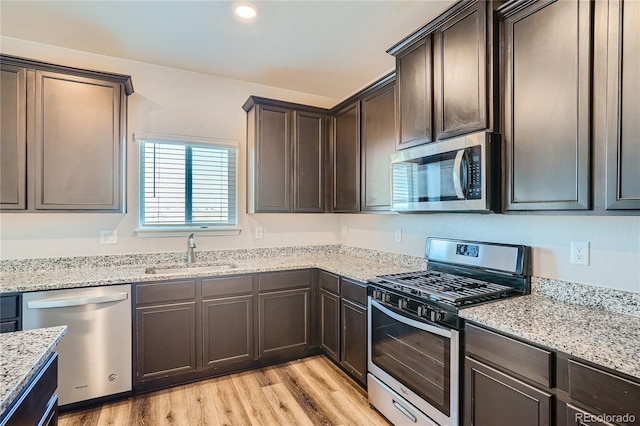 kitchen with sink, appliances with stainless steel finishes, light hardwood / wood-style floors, light stone counters, and dark brown cabinetry