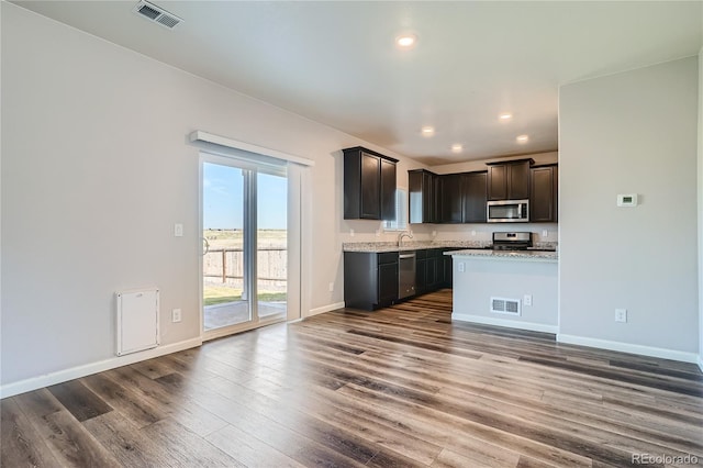 kitchen featuring dark brown cabinetry, light stone countertops, wood-type flooring, and appliances with stainless steel finishes