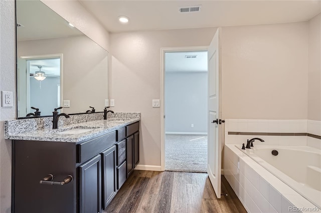 bathroom featuring hardwood / wood-style floors, vanity, ceiling fan, and tiled tub