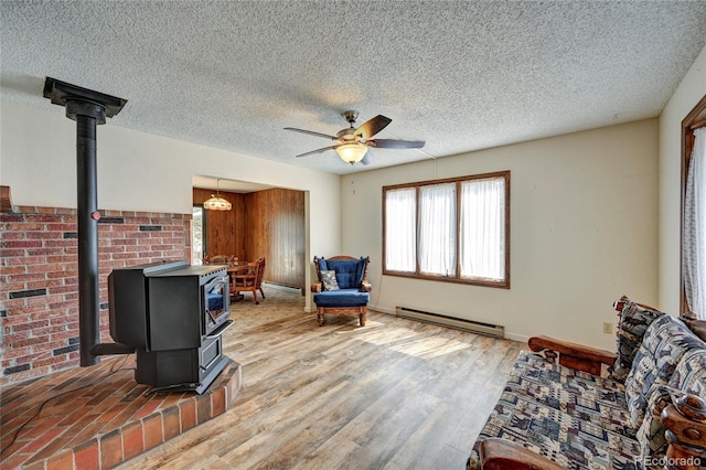 sitting room with a textured ceiling, ceiling fan, hardwood / wood-style flooring, a baseboard radiator, and a wood stove