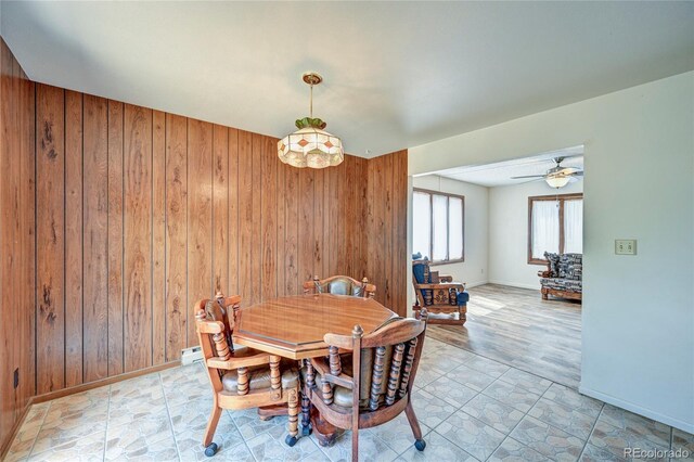 dining area featuring light wood-type flooring, ceiling fan, and wood walls