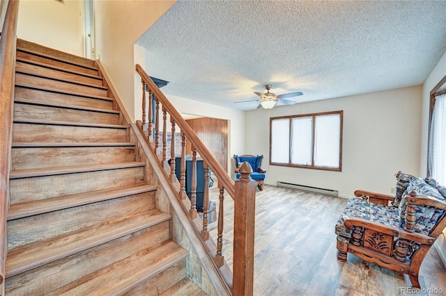 stairway with hardwood / wood-style floors, a textured ceiling, ceiling fan, and a baseboard heating unit