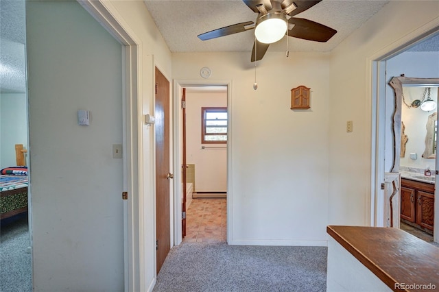 hall with baseboard heating, light carpet, sink, and a textured ceiling