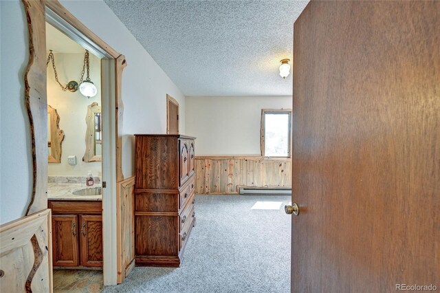 corridor featuring a baseboard heating unit, sink, wooden walls, a textured ceiling, and light colored carpet