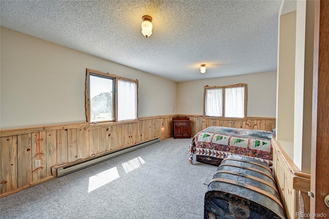 bedroom with wooden walls, light colored carpet, a baseboard radiator, and a textured ceiling