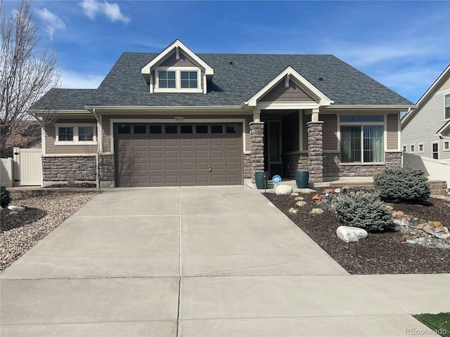 craftsman-style house with an attached garage, fence, stone siding, driveway, and roof with shingles