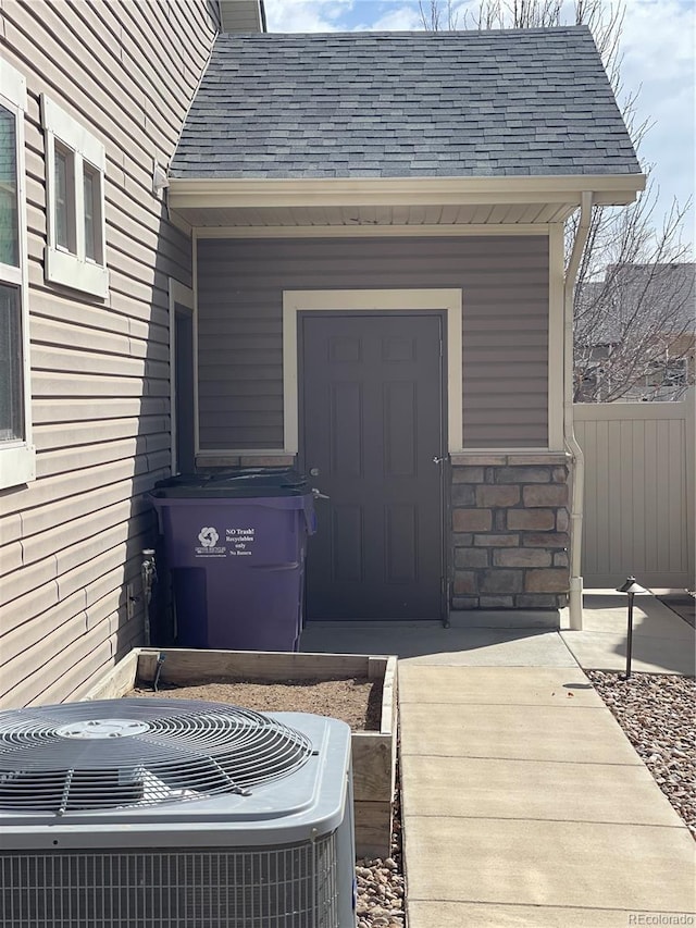 property entrance with a shingled roof, fence, and central AC unit