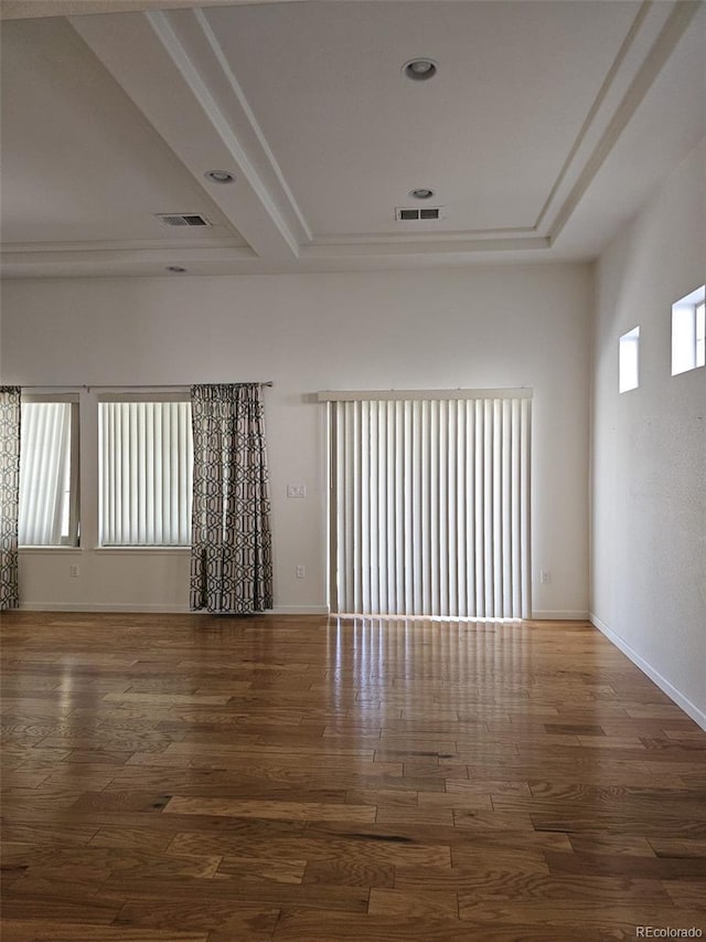 spare room with baseboards, visible vents, a tray ceiling, and wood finished floors