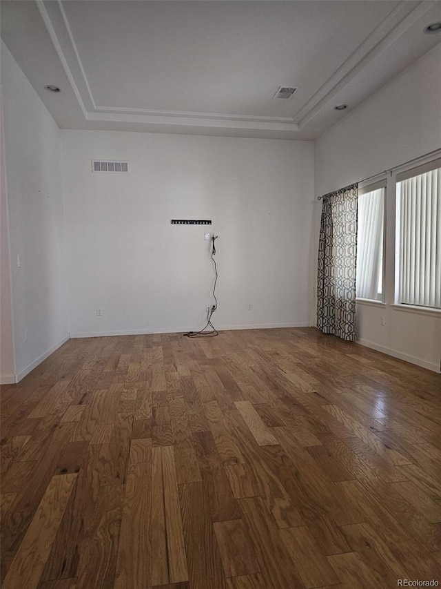 spare room with a tray ceiling, visible vents, baseboards, and wood finished floors