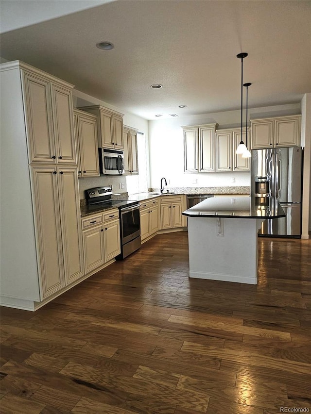 kitchen featuring cream cabinetry, decorative light fixtures, dark wood finished floors, dark countertops, and appliances with stainless steel finishes