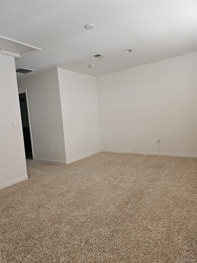 empty room featuring carpet floors, visible vents, a textured ceiling, and baseboards