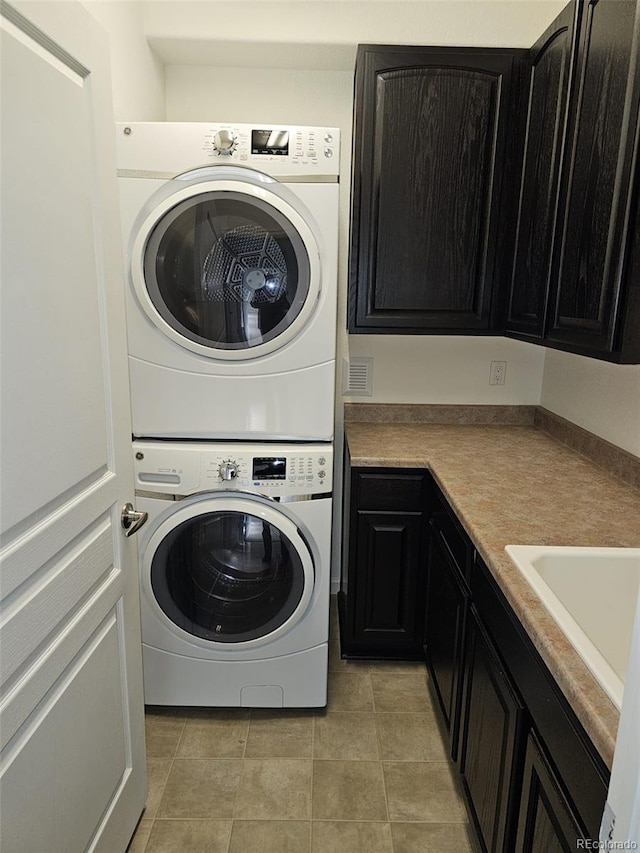 laundry room featuring cabinet space, a sink, stacked washing maching and dryer, and light tile patterned flooring