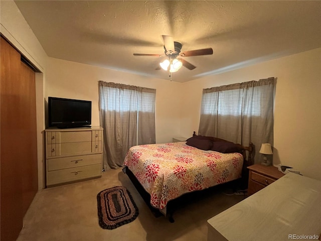 bedroom with ceiling fan, a closet, light carpet, and a textured ceiling