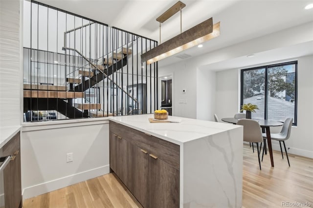 kitchen with light stone counters, dark brown cabinets, kitchen peninsula, and light wood-type flooring