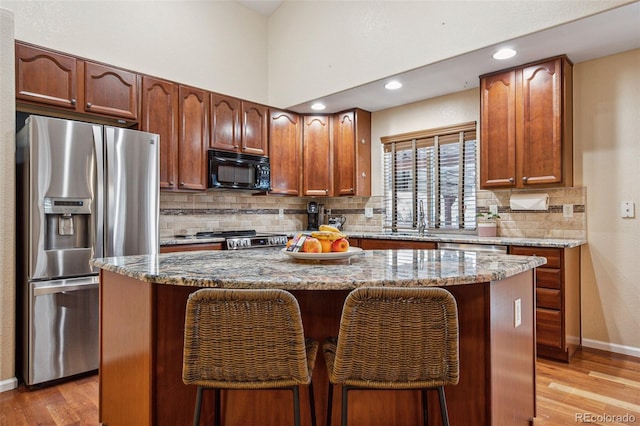 kitchen with stone counters, light wood-style flooring, black microwave, stainless steel fridge with ice dispenser, and decorative backsplash