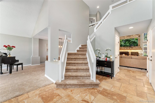 stairs featuring baseboards, a high ceiling, stone tile flooring, a stone fireplace, and carpet flooring