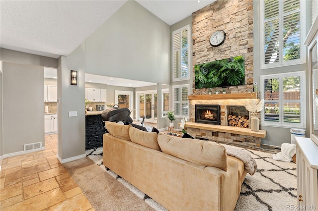 living room with baseboards, visible vents, a high ceiling, stone tile flooring, and a fireplace