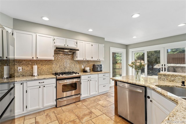 kitchen featuring appliances with stainless steel finishes, white cabinets, under cabinet range hood, and stone tile floors