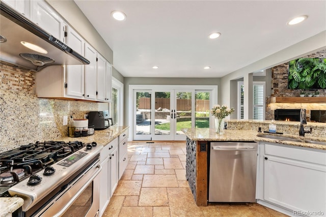 kitchen featuring stone tile floors, recessed lighting, under cabinet range hood, a sink, and appliances with stainless steel finishes