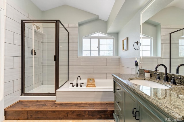 bathroom featuring a garden tub, vanity, tile walls, vaulted ceiling, and a stall shower