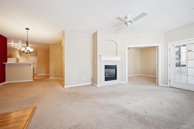 unfurnished living room featuring ceiling fan with notable chandelier, light colored carpet, and a fireplace