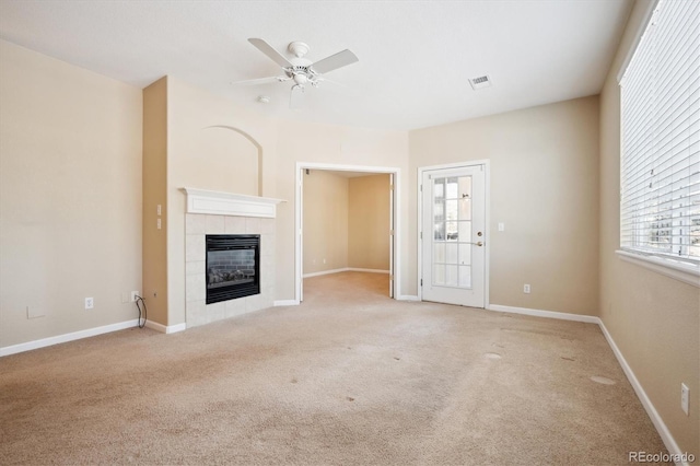 unfurnished living room with a tile fireplace, light colored carpet, and ceiling fan