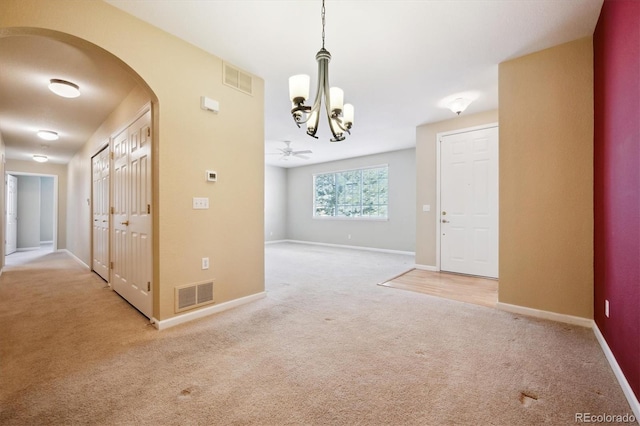 carpeted empty room featuring ceiling fan with notable chandelier