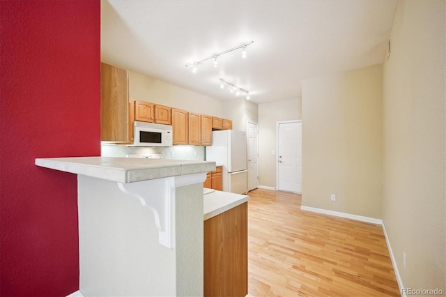 kitchen with rail lighting, a kitchen bar, kitchen peninsula, white appliances, and light hardwood / wood-style flooring