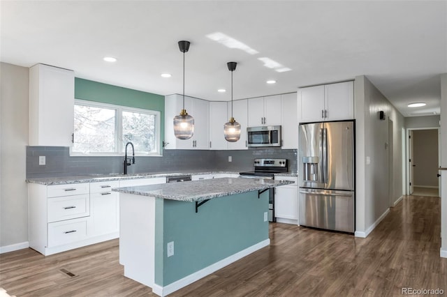 kitchen with appliances with stainless steel finishes, light stone counters, white cabinetry, pendant lighting, and a sink