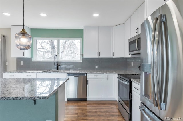 kitchen featuring light stone counters, pendant lighting, stainless steel appliances, white cabinets, and a sink