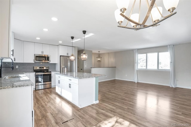 kitchen featuring a center island, stainless steel appliances, white cabinetry, pendant lighting, and a sink