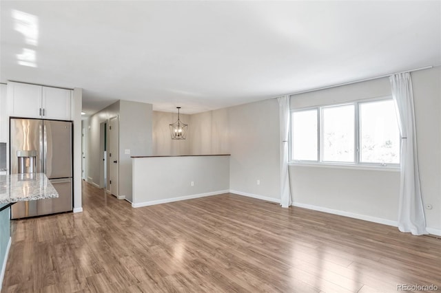 unfurnished living room featuring a chandelier, light wood-type flooring, and baseboards