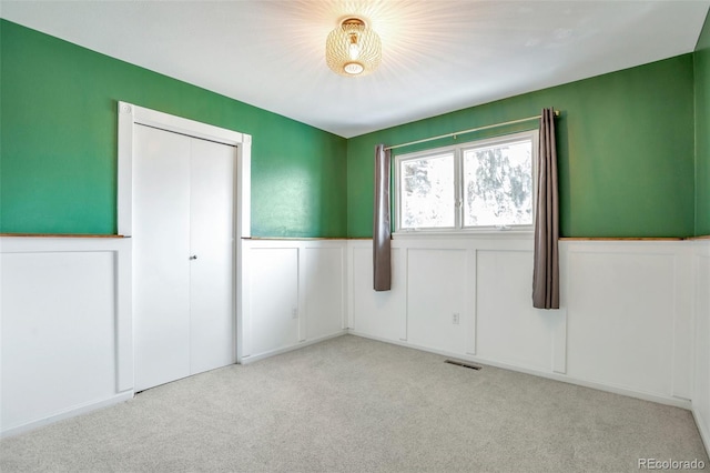 unfurnished bedroom with a closet, light colored carpet, a wainscoted wall, and visible vents