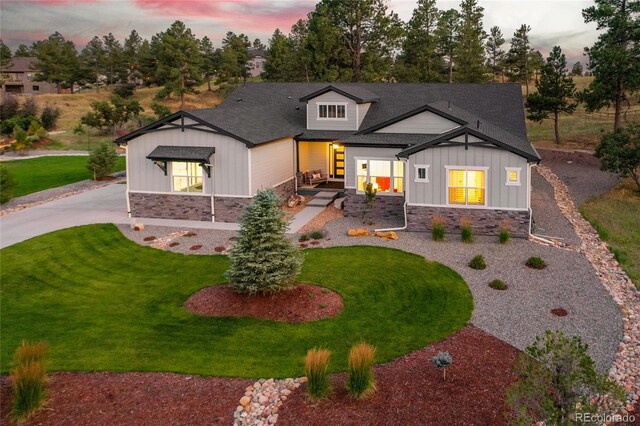 back of property featuring stone siding, board and batten siding, a yard, and curved driveway