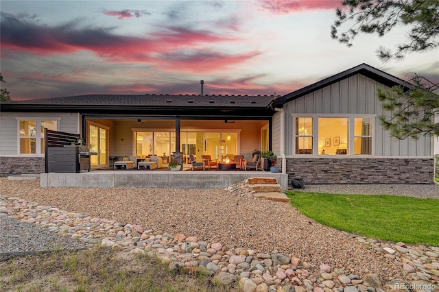 rear view of property featuring stone siding, a patio area, board and batten siding, and an outdoor living space