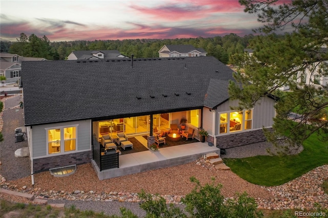 back of property at dusk with stone siding, a patio, and a shingled roof