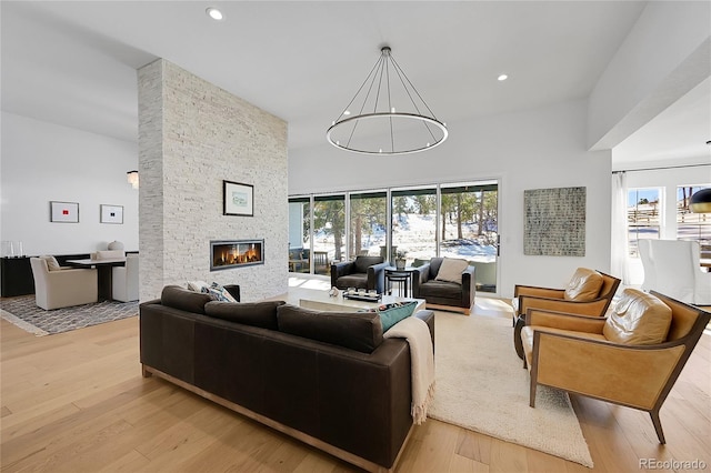 living area featuring plenty of natural light, a stone fireplace, a towering ceiling, light wood-style floors, and recessed lighting