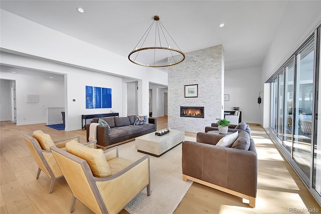 living area featuring light wood-type flooring, a fireplace, a towering ceiling, baseboards, and recessed lighting