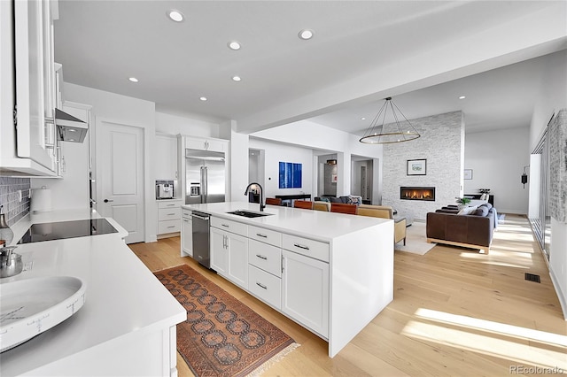 kitchen with a sink, appliances with stainless steel finishes, open floor plan, light wood-style floors, and recessed lighting
