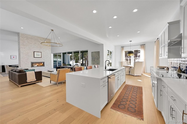 kitchen featuring a sink, stainless steel dishwasher, light wood-style flooring, recessed lighting, and a center island with sink