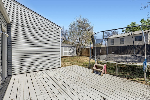 1958 Cathay Ct, Aurora, CO 80011 - wooden terrace featuring a trampoline, a fenced backyard, a storage shed, and an outdoor structure