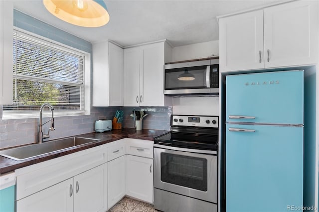 kitchen with dark countertops, a sink, white cabinetry, backsplash, and appliances with stainless steel finishes