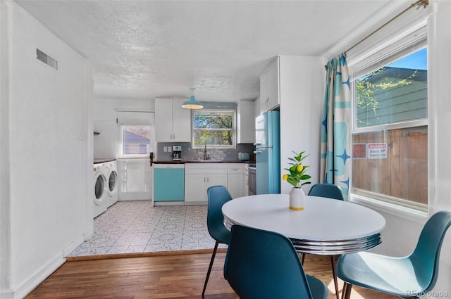 dining area with a textured ceiling, washer and clothes dryer, light wood-type flooring, baseboards, and visible vents