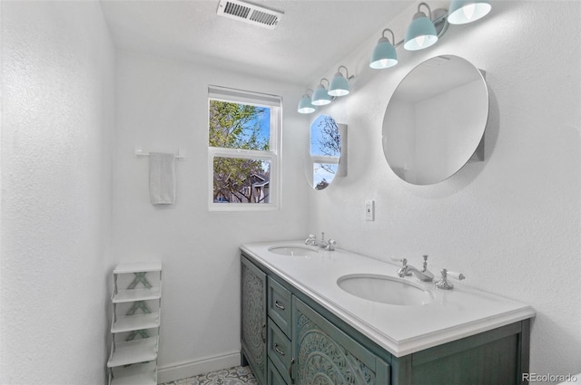 full bath with baseboards, visible vents, a sink, and double vanity