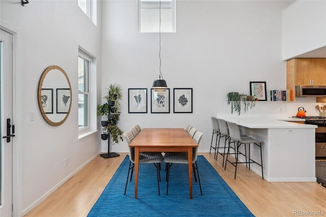 dining room with a towering ceiling, a healthy amount of sunlight, and light hardwood / wood-style floors