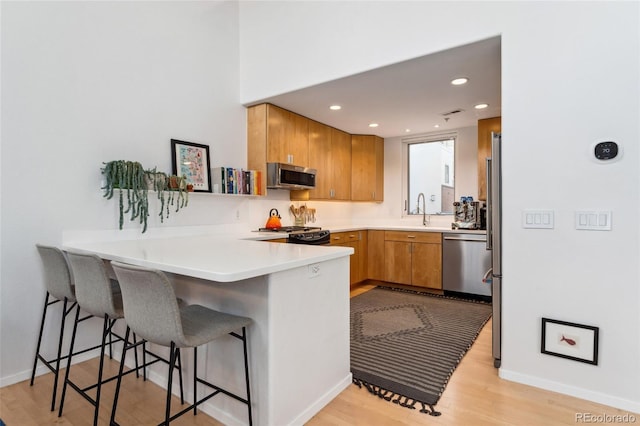 kitchen featuring sink, a breakfast bar area, kitchen peninsula, stainless steel appliances, and light wood-type flooring