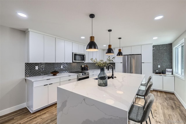 kitchen featuring a center island with sink, sink, white cabinetry, hanging light fixtures, and appliances with stainless steel finishes