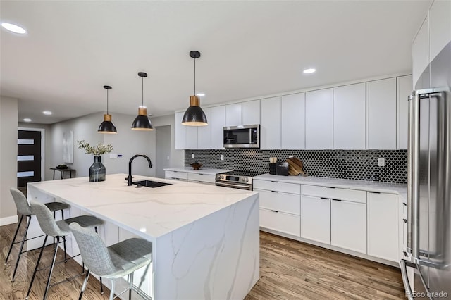 kitchen featuring white cabinetry, a center island with sink, appliances with stainless steel finishes, light stone countertops, and sink