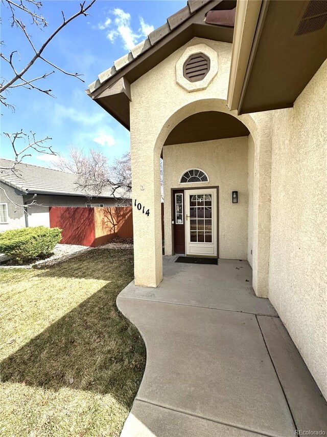 view of exterior entry featuring visible vents, fence, and stucco siding