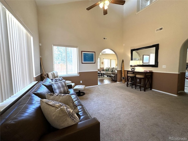 living area featuring visible vents, a ceiling fan, arched walkways, and carpet floors